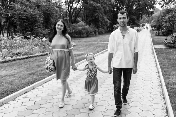 Щаслива сім'я йде по шляху тримаючи руки і проводячи час у прекрасному зеленому парку. Жінка вагітна . — стокове фото