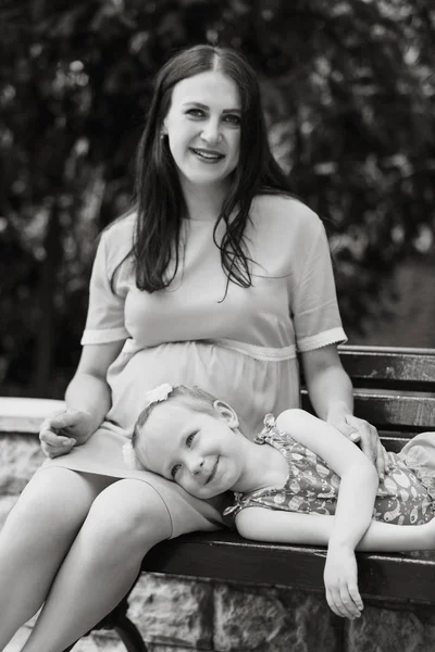 En gravid kvinna och en flicka som vilar på en bänk. Happy Family Life-konceptet. — Stockfoto