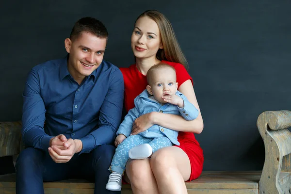 Föräldrar och deras barn sitter på en bänk. Mamma, pappa och barn. Porträtt av en ung familj. Ett lyckligt familjeliv. Människan föddes. — Stockfoto