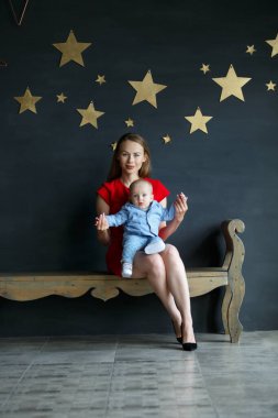 Anne ve çocuk bankta oturuyor. Genç bir ailenin portresi. Mutlu aile hayatı. Gri duvarda altın yıldızlar.