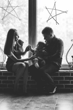 Ebeveynler ve çocukları pencerede oturuyorlar. Anne, baba ve bebek. Genç bir ailenin portresi. Mutlu aile hayatı. İnsanoğlu doğdu.