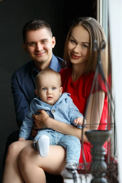 Parents and their child sitting at the window. Mom, dad and baby. Portrait of young family. Happy family life. Man was born. — Stockfoto