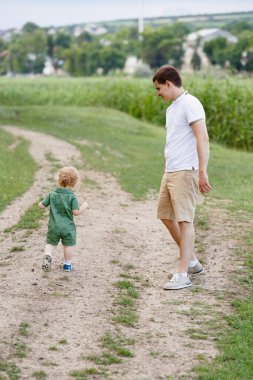 Sazlıkların arka planında yürüyen sevimli küçük bir çocuk. Babası da onunla birlikte. Parkta yürü. Aile hayatı. Dikey çerçevelenmiş çekim.