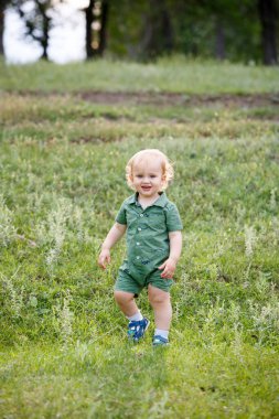 Küçük bir çocuk çimlerin arasında koşuyor. Parkta yürü. Dikey çerçevelenmiş çekim.