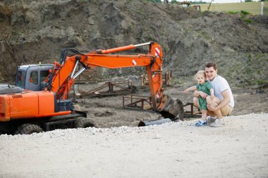 İnşaat alanında genç bir baba ve oğul. Kazıcıya hayranlar. Yatay çerçeveli çekim.