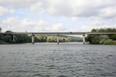 Nehir köprüsü. Sabit bir su akışı. Nehrin iki yakasında da ağaçlar var. Yatay çerçeveli çekim.