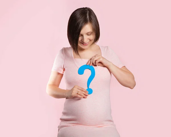 A pregnant woman at 22 weeks of pregnancy. Figure of a pregnant woman in a pink dress on a pink background with a blue question mark. Determining the baby\'s gender. A boy or a girl.