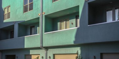 Güneşli balkon ve cam pencereler ile bina. Bir yeşil onun duvar aydınlatma güneş ile bina dış görünümünü. Bina ile lambalar ve dikdörtgen cam pencere balkon vardır.