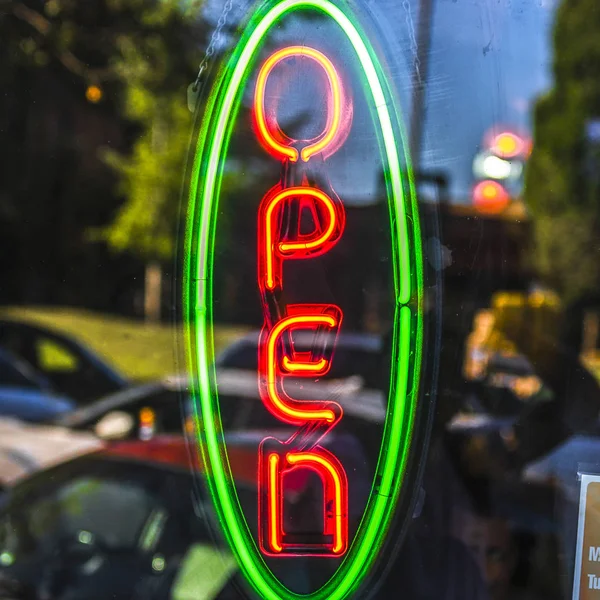 Cartel abierto de neón en una puerta de cristal con reflejos — Foto de Stock