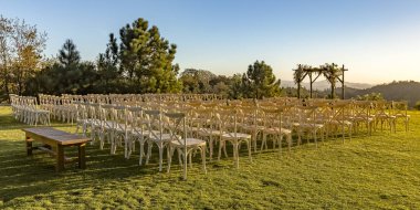 Sandalye ve görünüm çarpıcı bir çimenlikte huppah. Beyaz sandalye ve Yahudi bir düğün için Chuppah bakımlı bir bahçede yer. Alan, ağaç, dağ ve gökyüzü çarpıcı bir görünüm tarafından çevrilidir.