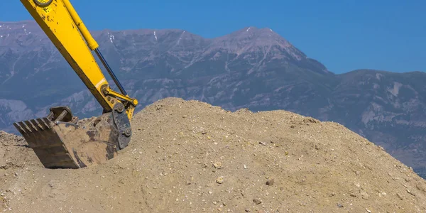 Excavator arm scooping dirt in front of mountain — Stock Photo, Image