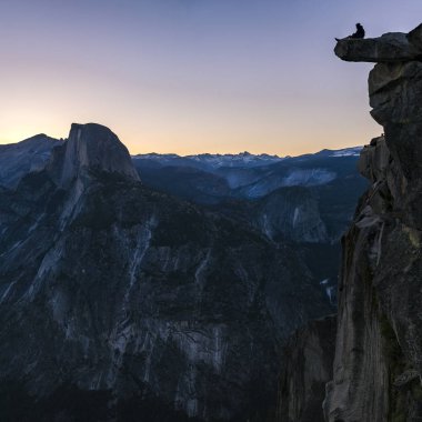 Yosemite bir uçurumun kenarında oturan adam