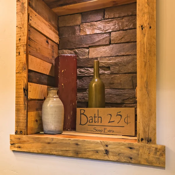 Bath sign on a wooden and brick wall alcove. Wooden sign board reading Bath 25 cents and soap extra inside a wall alcove. The alcove has a wood and brick wall with a green bottle and vase inside.