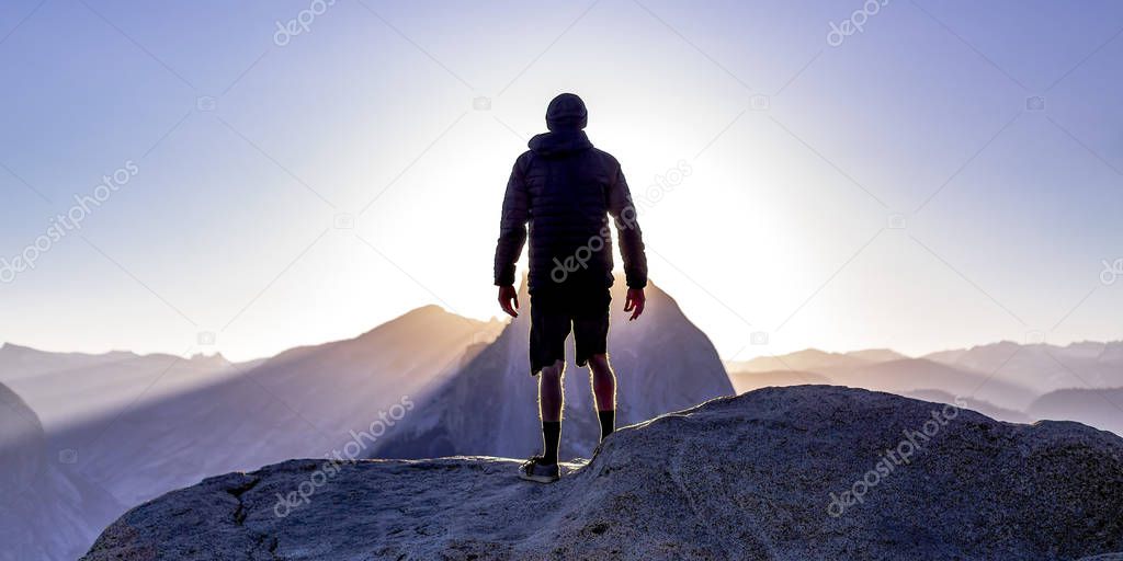 Man on a cliff with view of sun and mountains