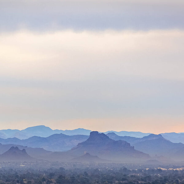 Mountain range of Arizona beneath a misty sky. Scenic view of the rugged mountains of Arizona beneath a misty vast sky. Trees and the city can be seen at the foot of the imposing mountains.