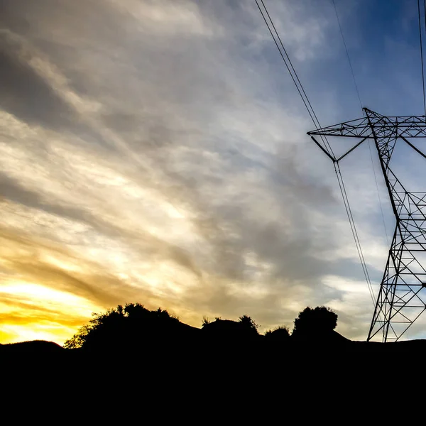 Power line on hill silhouetted against cloudy sky