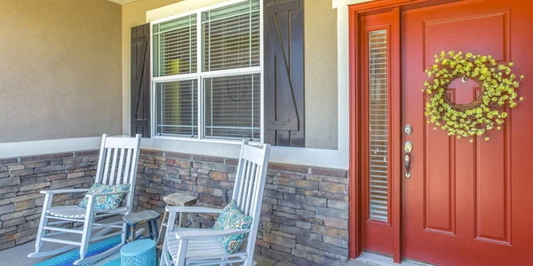 Red front door with wreath and chairs on porch