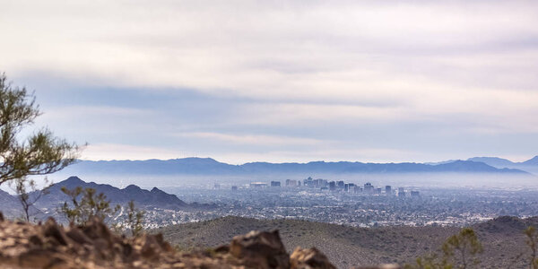Scenic view of the populous Phoenix in Arizona. Expansive view of the populous city of Phoenix in Arizona. Incredible mountains surround the cityscape beneath a vast cloudy sky.