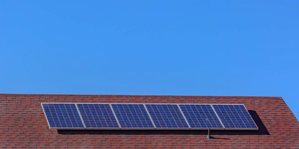 Солнечные панели на красной крыше под чистым голубым небом — стоковое фото