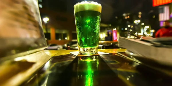 El vaso con el líquido brillante verde sobre la mesa por la noche —  Fotos de Stock