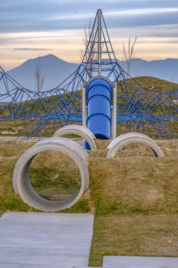 Çocuk ve oyun alanında arkasında bir slayt ve halat tırmanma beton tünellere. Çimenli hills tüneller var ve gün batımında dağların arkasında bir görünüm.