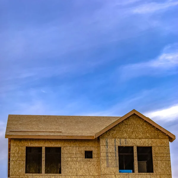 Front roof of home under construction copy space above the home in the blue sky with some clouds. The home is being built and is currently a wooden structure with ply wood in Daybreak Utah.