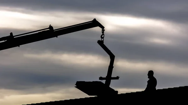 Silhouet van een kraan en de man op het dak van huis — Stockfoto