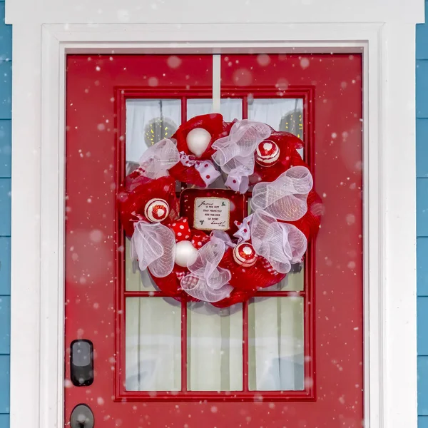 Red front door with wreath viewed on a snowy day