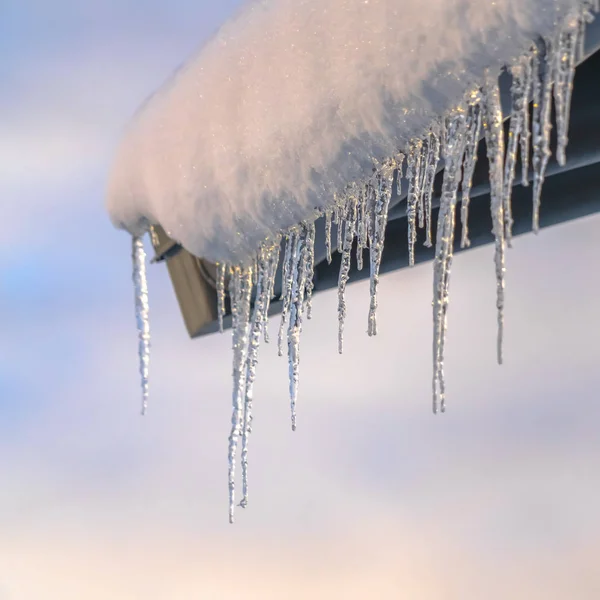 Snow covered roof with icicles against cloudy sky