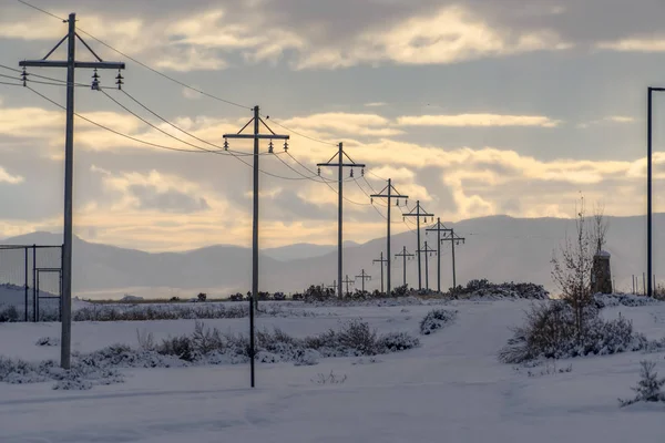 Power lines on snowy road against mountain and sky