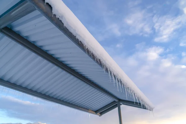 Telhado nevado com icicles contra céu azul nublado — Fotografia de Stock