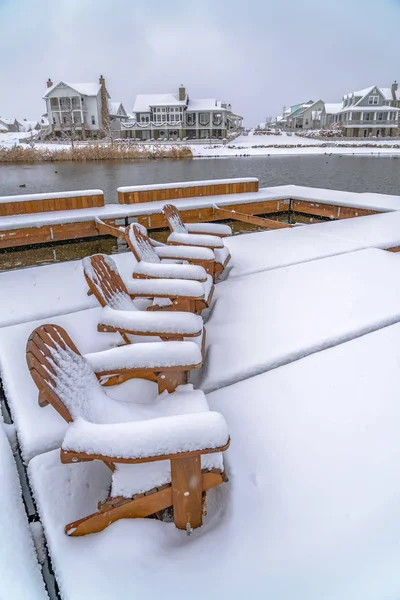 Snowy chairs on lake deck with view of homes