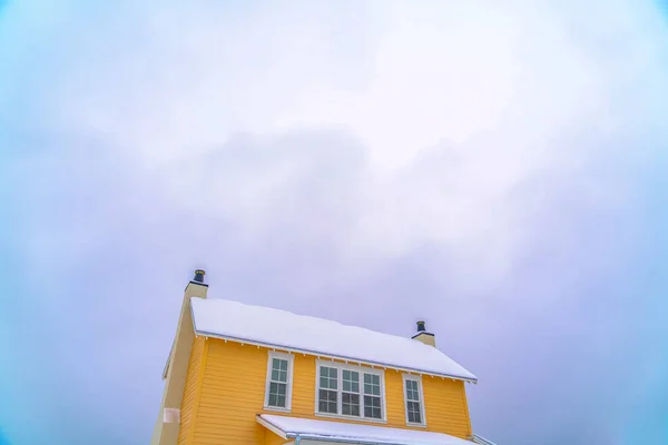 Casa amarilla con techo cubierto de nieve contra el cielo — Foto de Stock