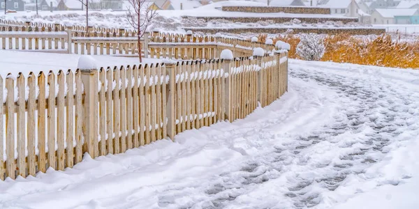 Footsteps on snow along a wooden fence in Daybreak