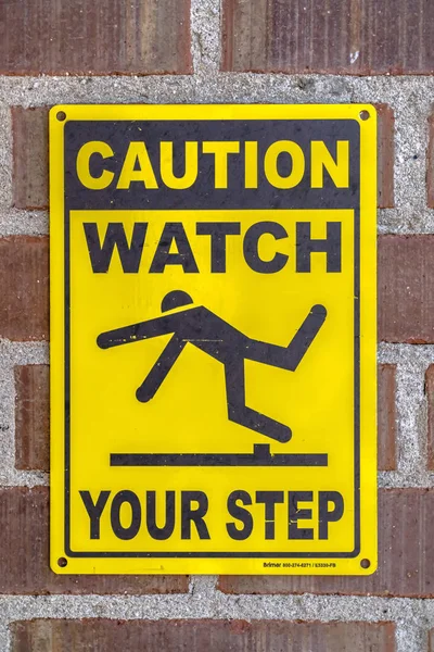 Caution Watch Your Step sign on a brick wall