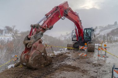 Kışın görülen barikatlar ve sarı bant ile çamurlu bir yolda ekskavatör