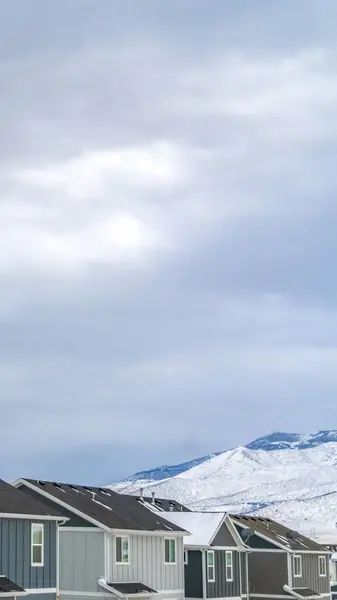 Linha Vertical clara de casas contra a montanha coberta de neve sob o céu cheio de nuvens — Fotografia de Stock