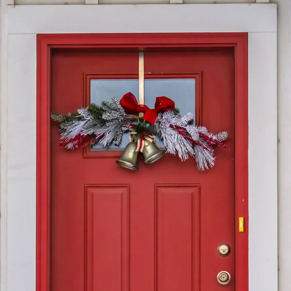 Square Front door with glass panel and holiday decoration against a ribbed white wall