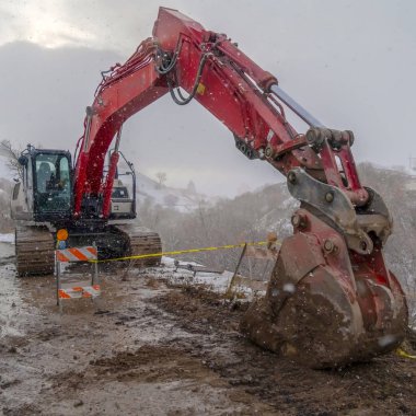 Kışın görülen çamurlu bir dağ yolunda kırmızı ekskavatör ve barikat