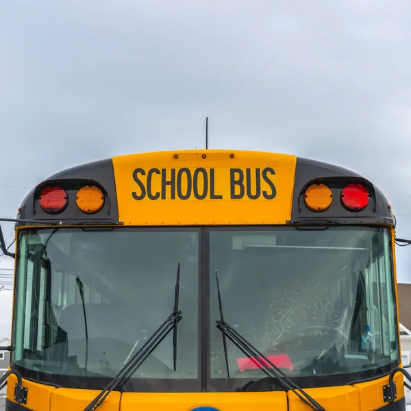 Clear Square Front view of a yellow school bus with homes and cloudy sky in the background