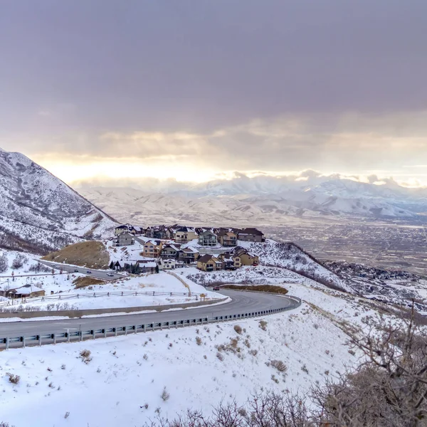 Clear Square Road curving along a mountain coated with snow against cloudy sky in winter