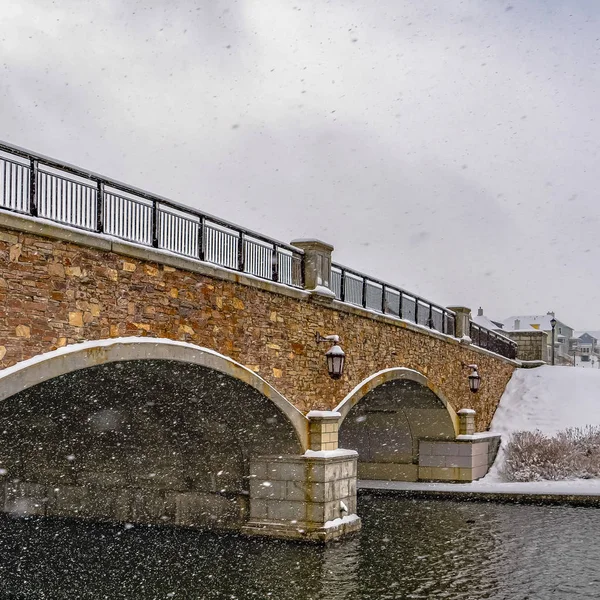 Square Stone arched bridge with lamps over a lake during winter in Daybreak Utah