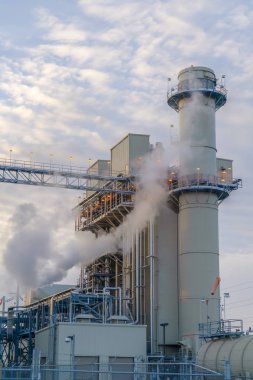 Kulenin arkasında kabarık bulutlar ve bir Elektrik Santrali binaları ile mavi gökyüzü