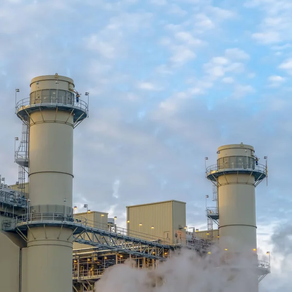 Vierkant bewolkt blauwe hemel gezien achter de torens en gebouwen van een elektriciteitscentrale — Stockfoto