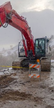Kışın görülen barikatlar ve sarı bant ile çamurlu bir yolda Dikey Ekskavatör