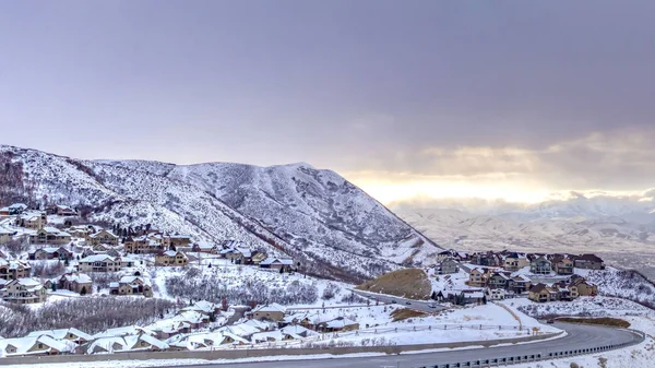 Route panoramique dégagée courbant le long d'une montagne recouverte de neige contre un ciel nuageux en hiver — Photo