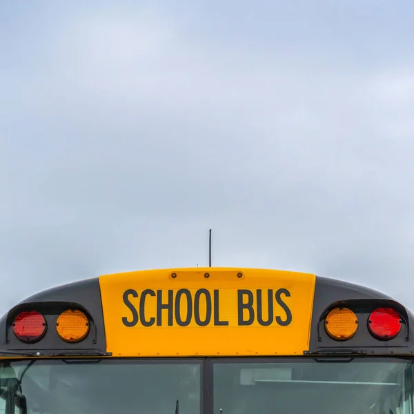 Kwadratowy widok z przodu żółtego autobusu szkolnego z domów i pochmurne niebo w tle — Zdjęcie stockowe