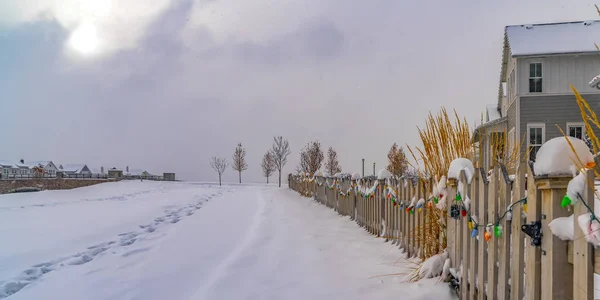 Sendero en el suelo cubierto de nieve a lo largo de una valla con luces de colores en invierno — Foto de Stock