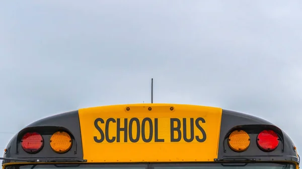 Panorama Vista frontal de um ônibus escolar amarelo com casas e céu nublado no fundo — Fotografia de Stock