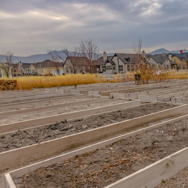 Square Raised garden beds with homes and mountain against cloudy sky in the background